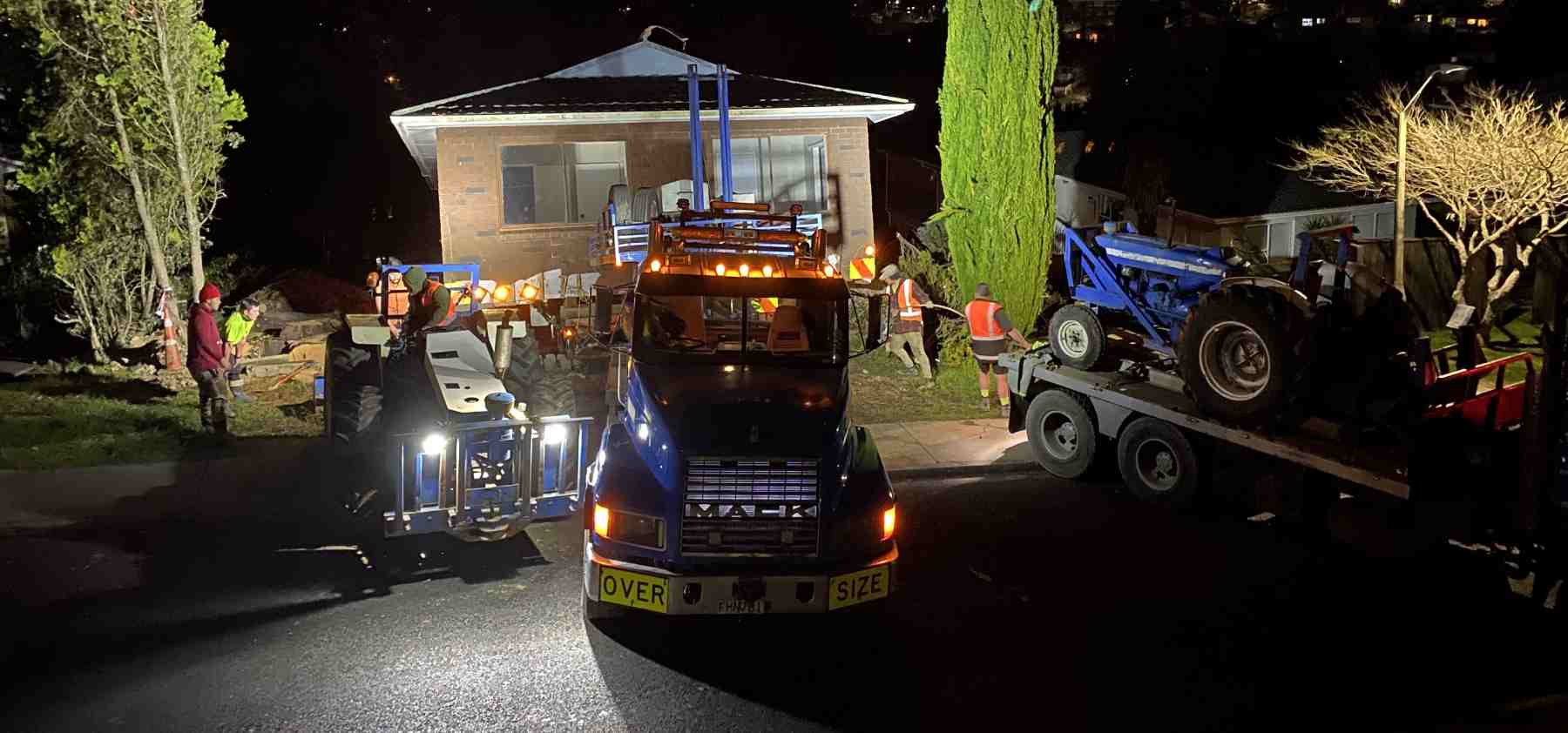 Workers and large trucks with machinery for house removal at night.