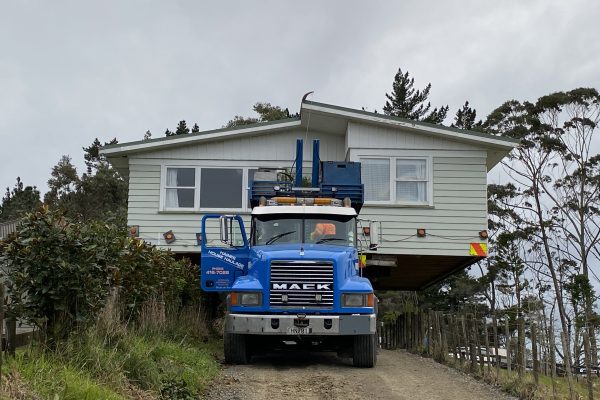 A weatherboard home loaded on the back of a Mack truck getting ready to be moved