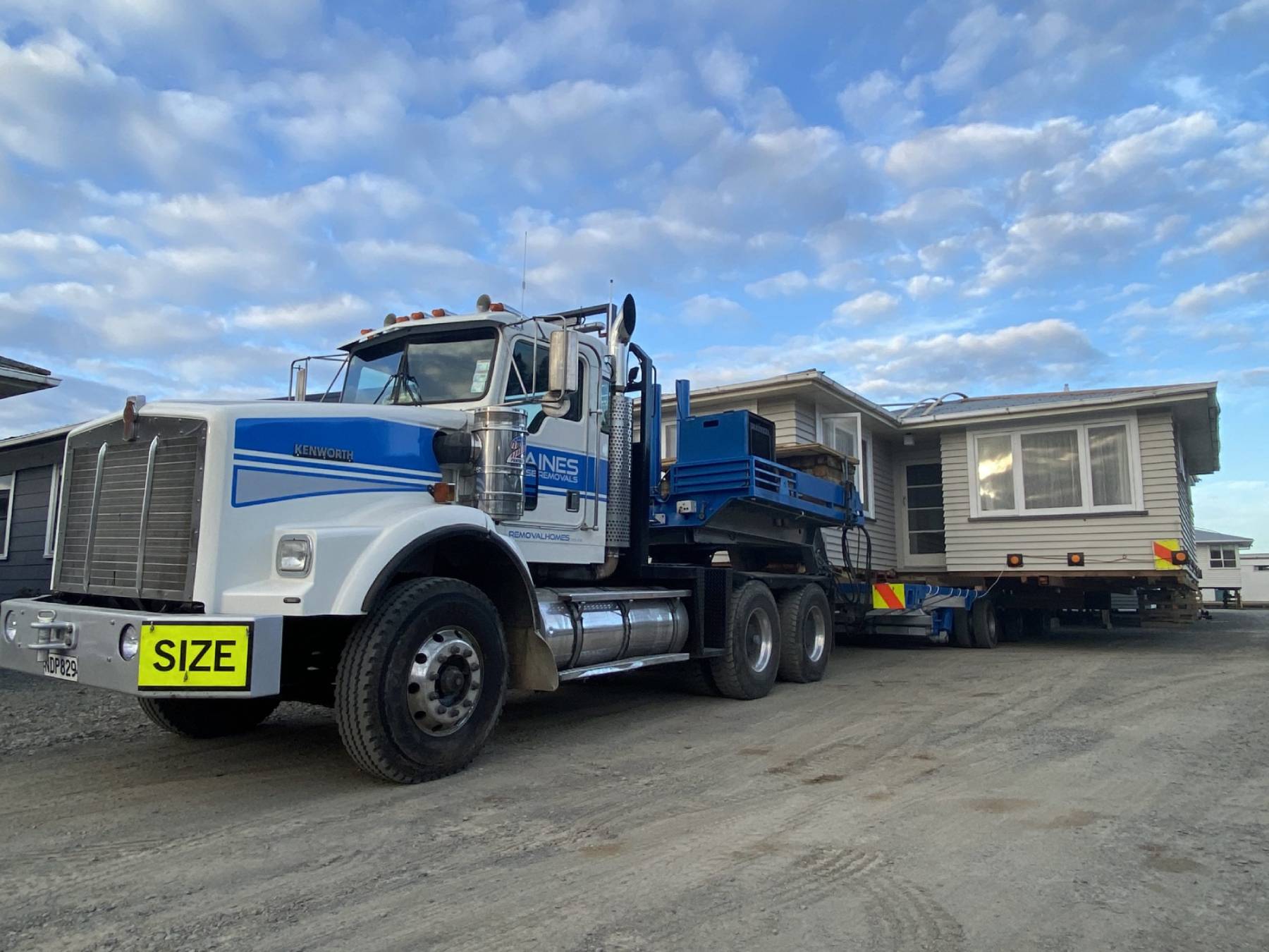Housemoving Kenworth truck with Haines House Removal signwriting and wide house on back of trailer
