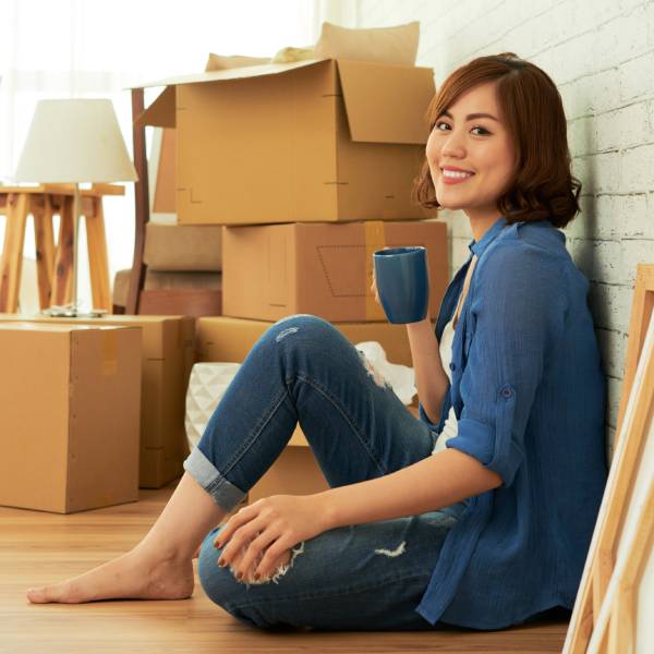 Lady sitting and relaxing while drinking coffee with boxes packed in background for moving